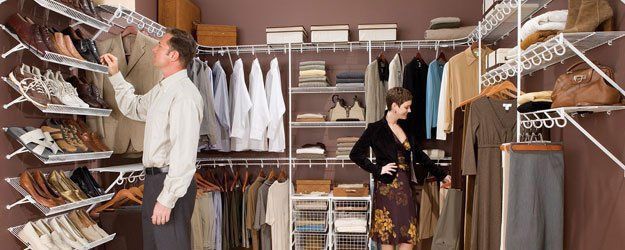 A man and a woman are standing in a walk in closet.