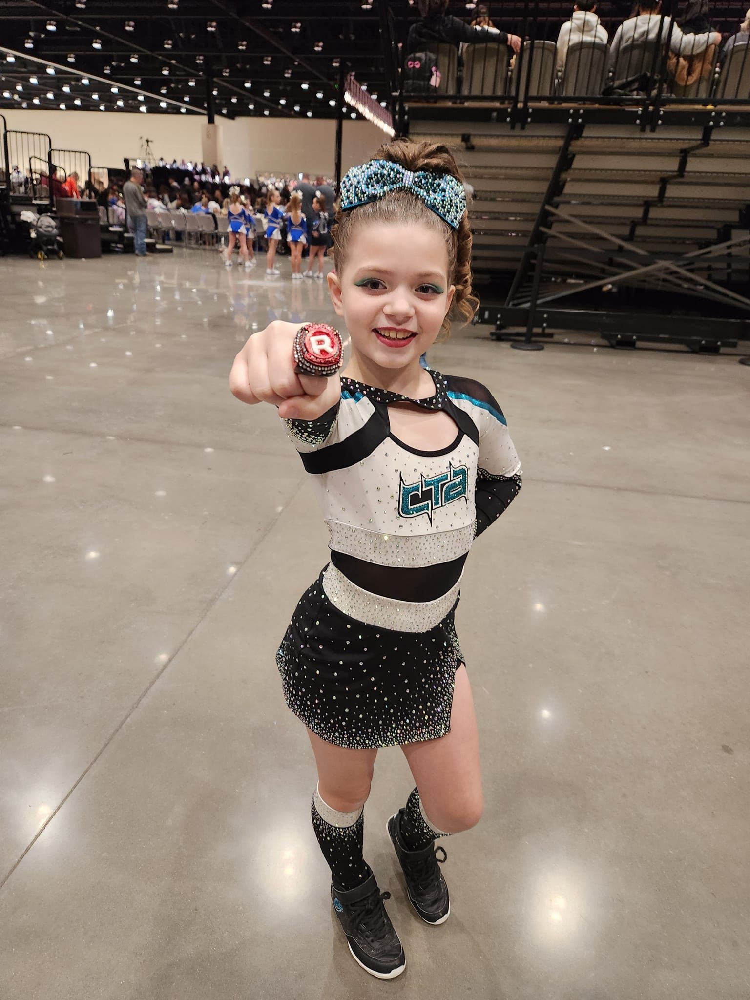 A young girl in a cheerleading uniform is pointing at the camera.