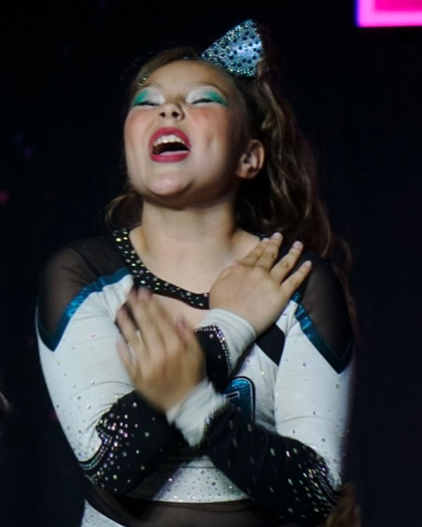 A cheerleader with a bow on her head is clapping her hands