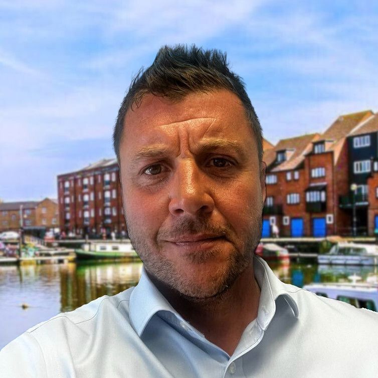 A man in a white shirt is standing in front of a body of water.
