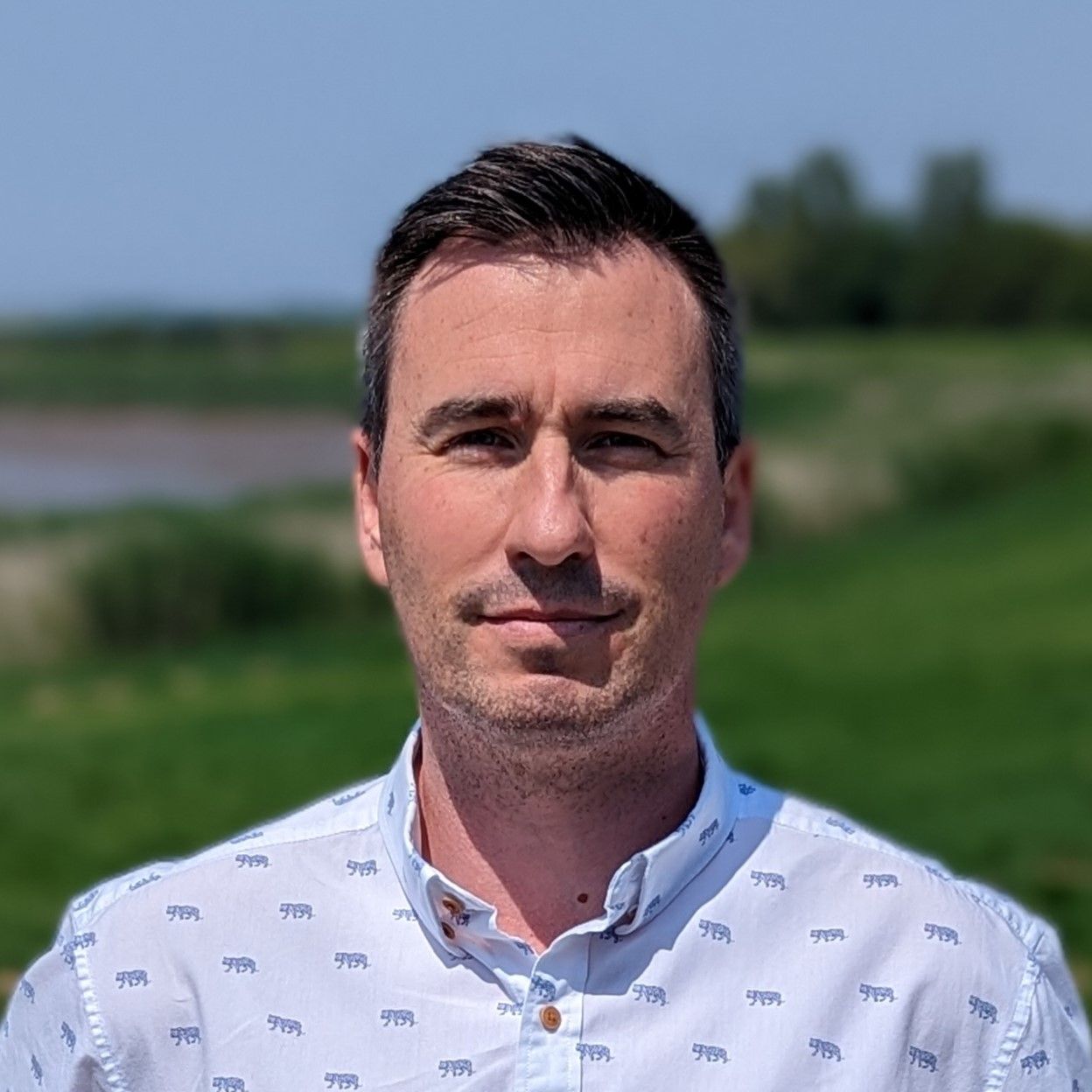A man in a white shirt is standing in front of a field.