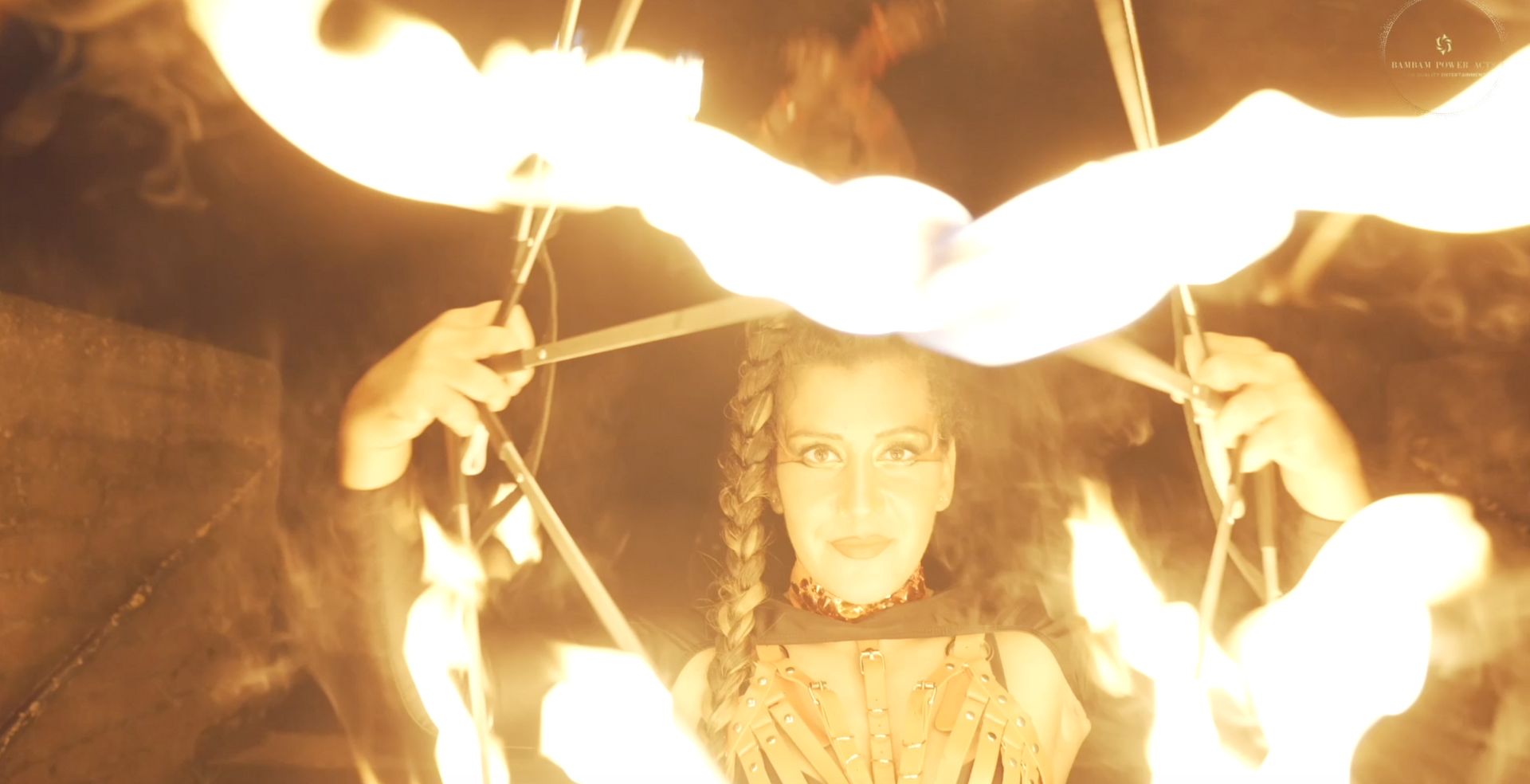 Woman surrounded by fire, arms raised. Bright flames form a pentagram above her head.
