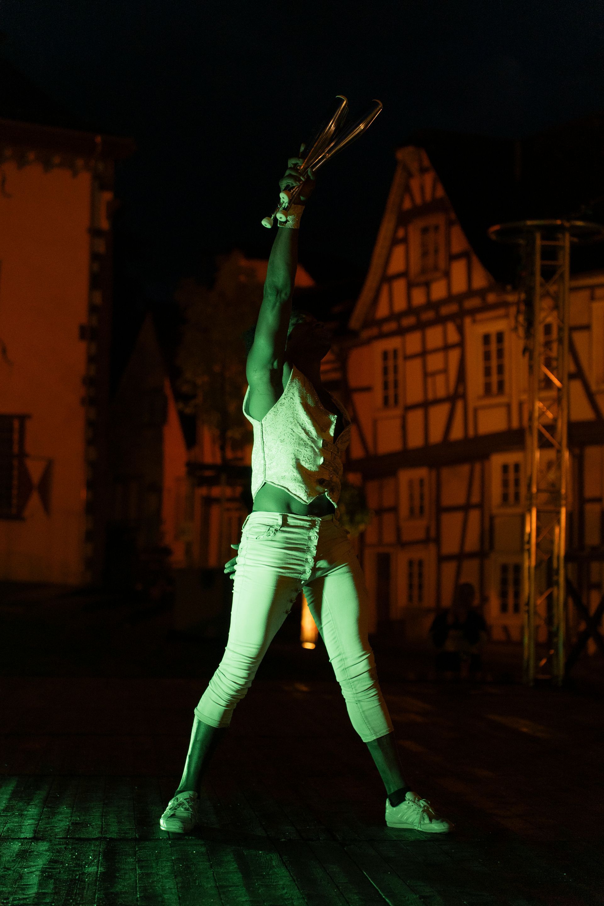 Two women in fairy costumes dance in a town square, illuminated by the setting sun, watched by an audience.
