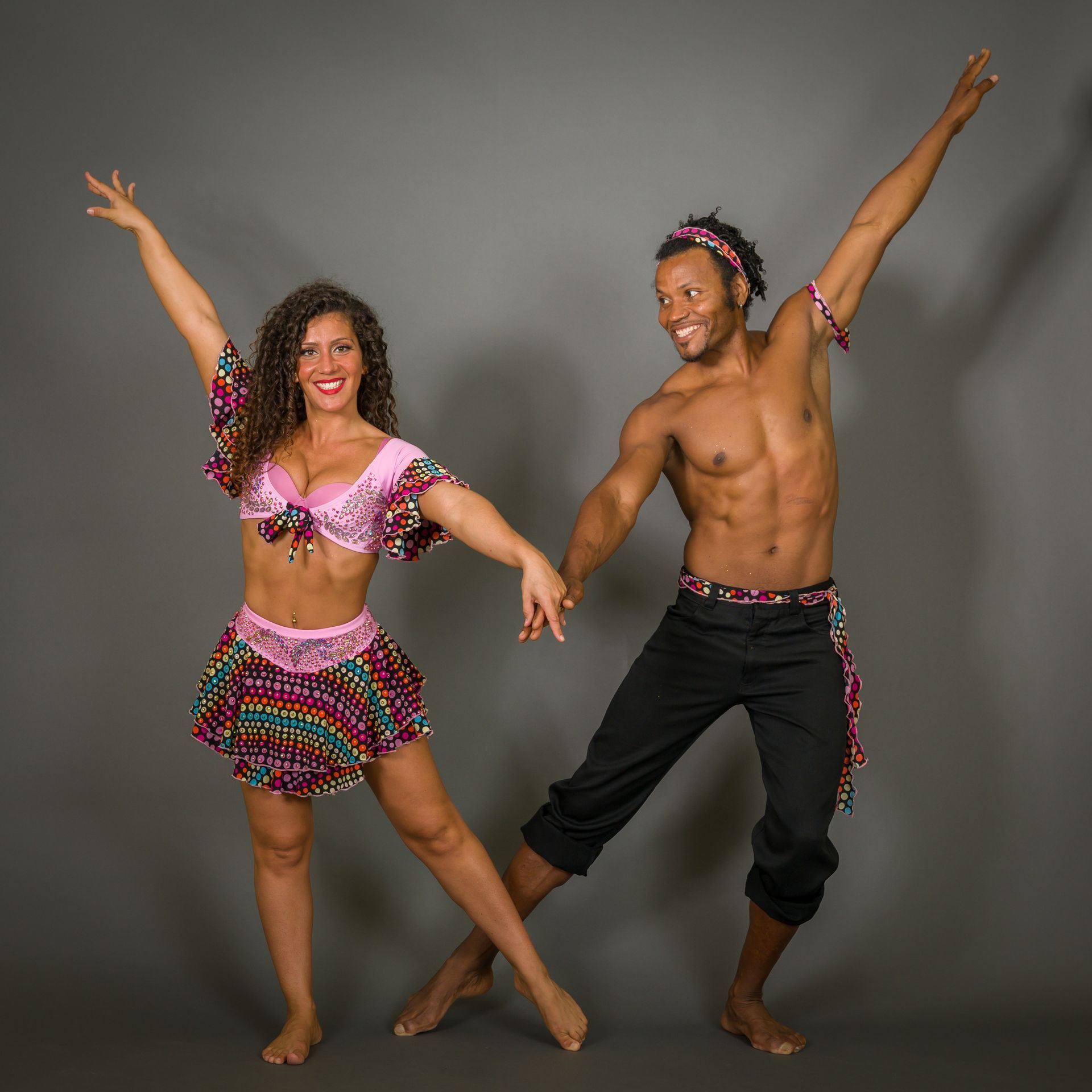 Two dancers in colorful outfits, holding hands, striking poses with arms raised.