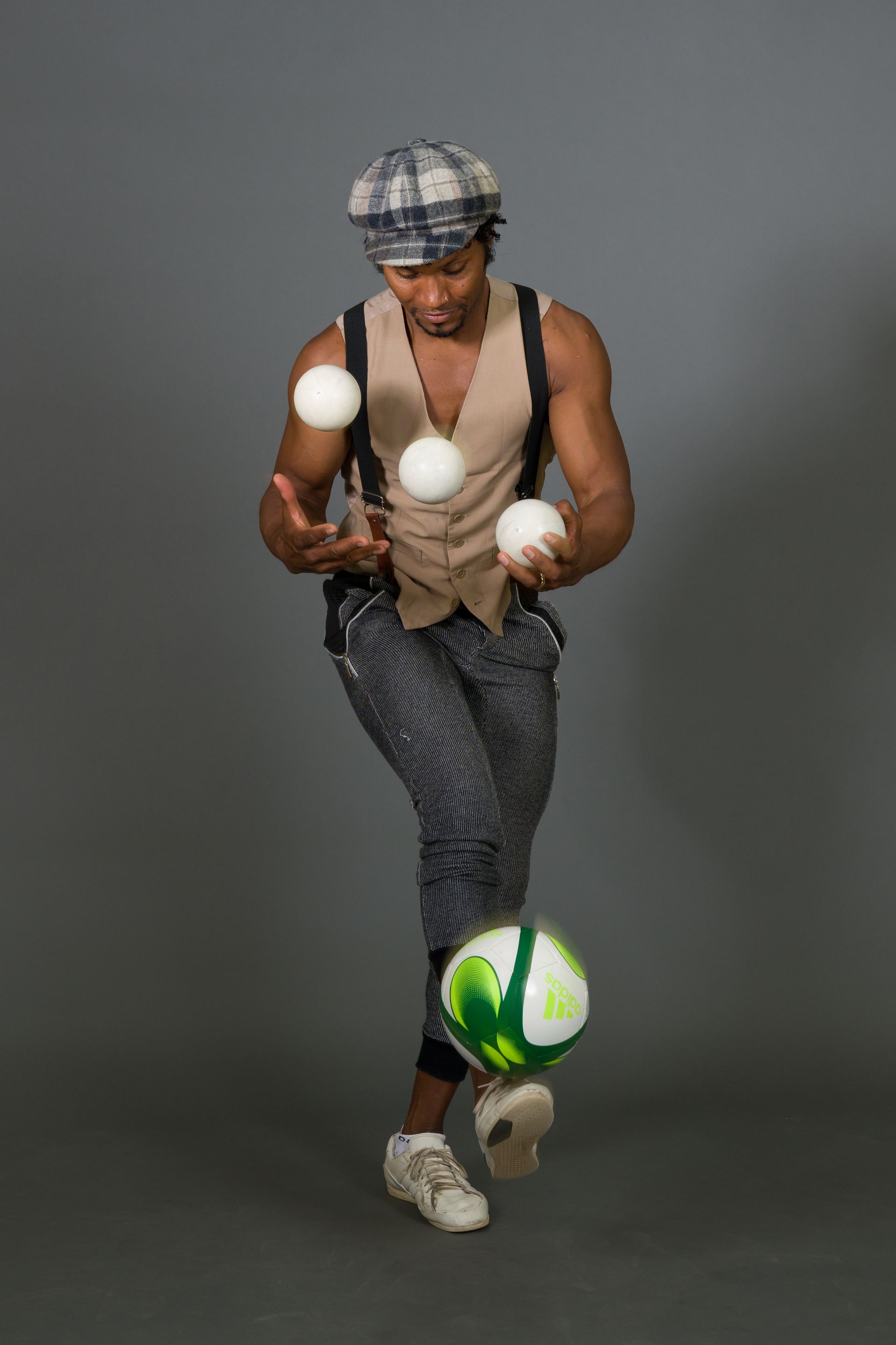 Man juggling three white balls and a soccer ball against a gray backdrop.