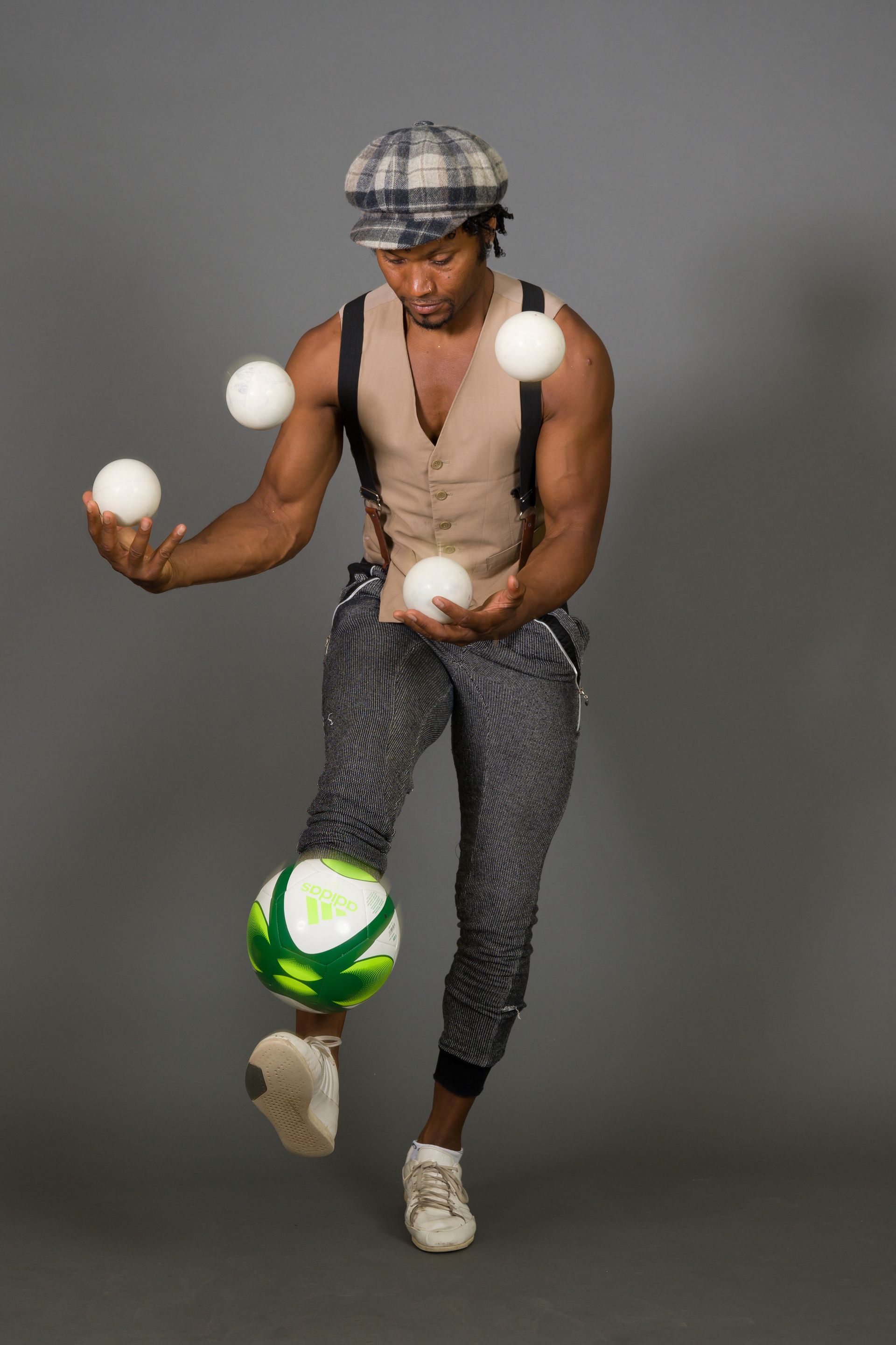 Man juggling four white balls and a soccer ball with his foot.