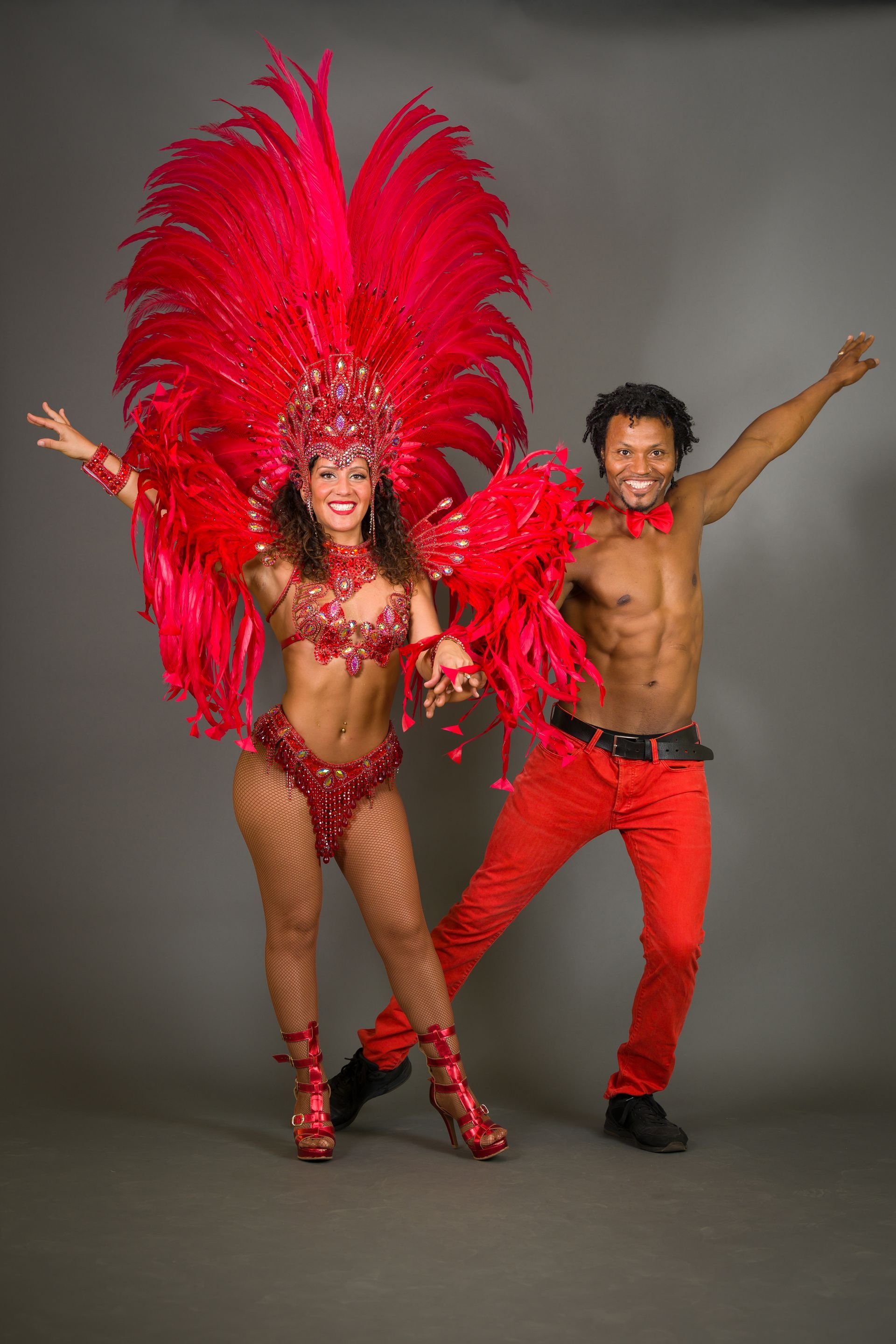 Man and woman in red samba costumes posing. Gray backdrop.