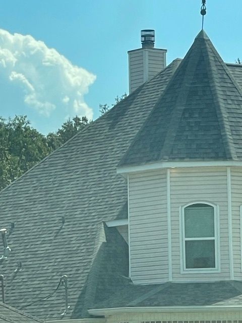 Tan house with brown shingled roof, white trim, and blue window reflections.