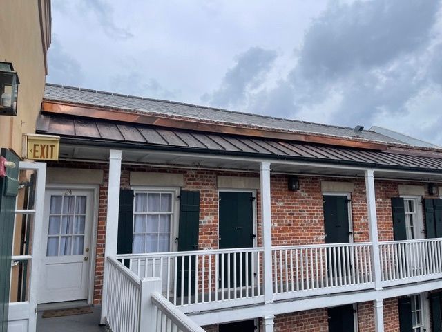 Gray metal roof on a house with a gutter and chimney, set against green trees.