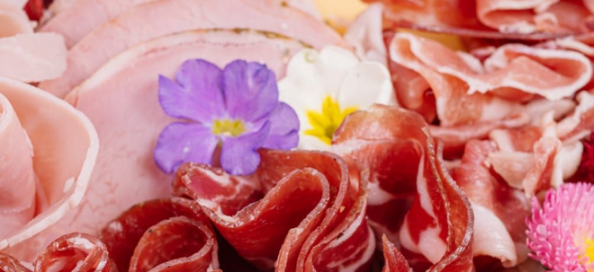 Primer plano de una tabla de charcutería con rodajas de carne y flores comestibles.