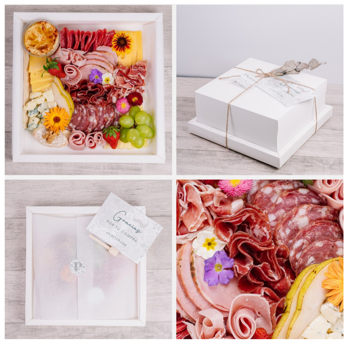 Tabla de charcutería en caja blanca con carnes, quesos, frutas y flores; empaquetada y lista para regalar.