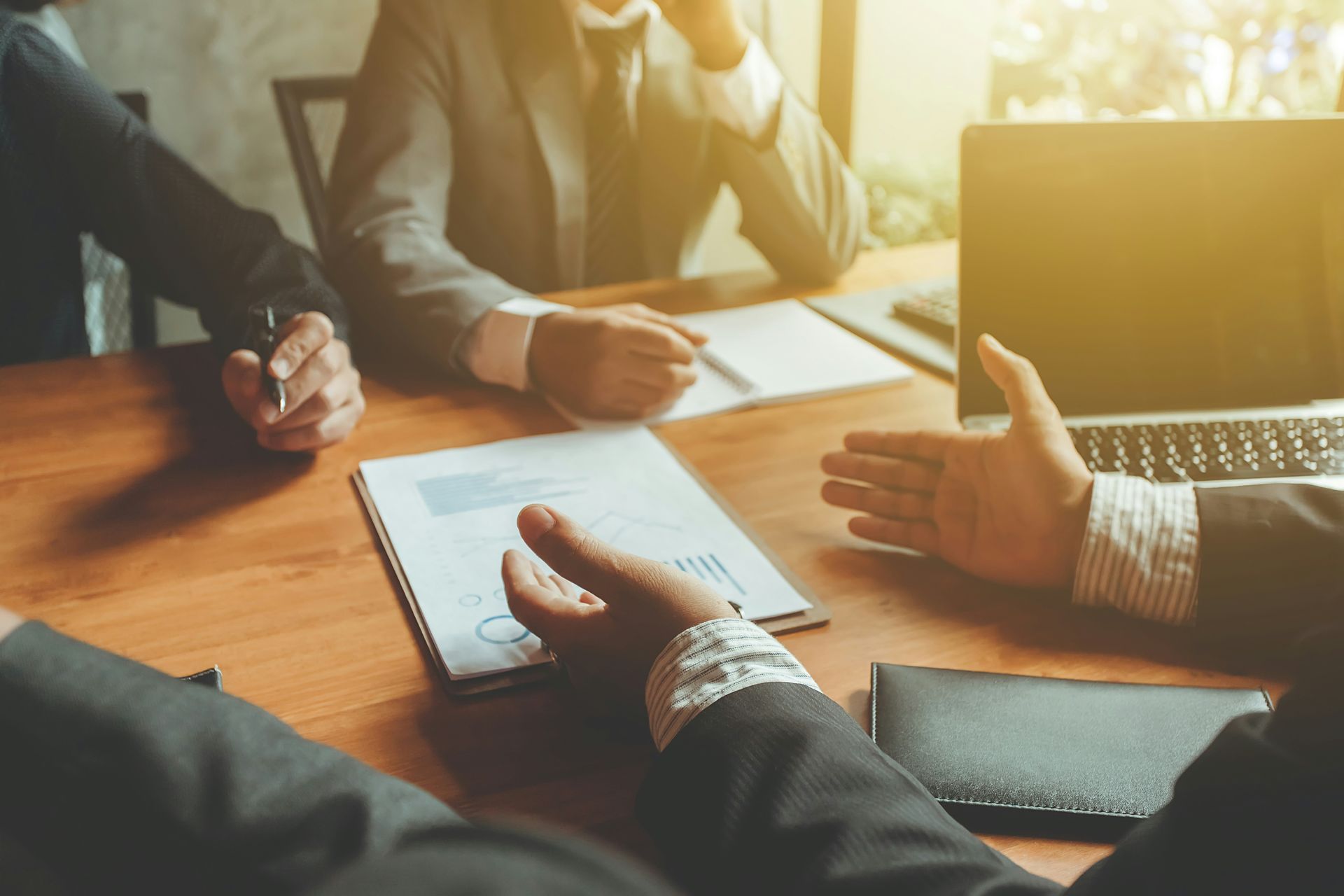 Business meeting with three people around a wooden table discussing documents and laptop.