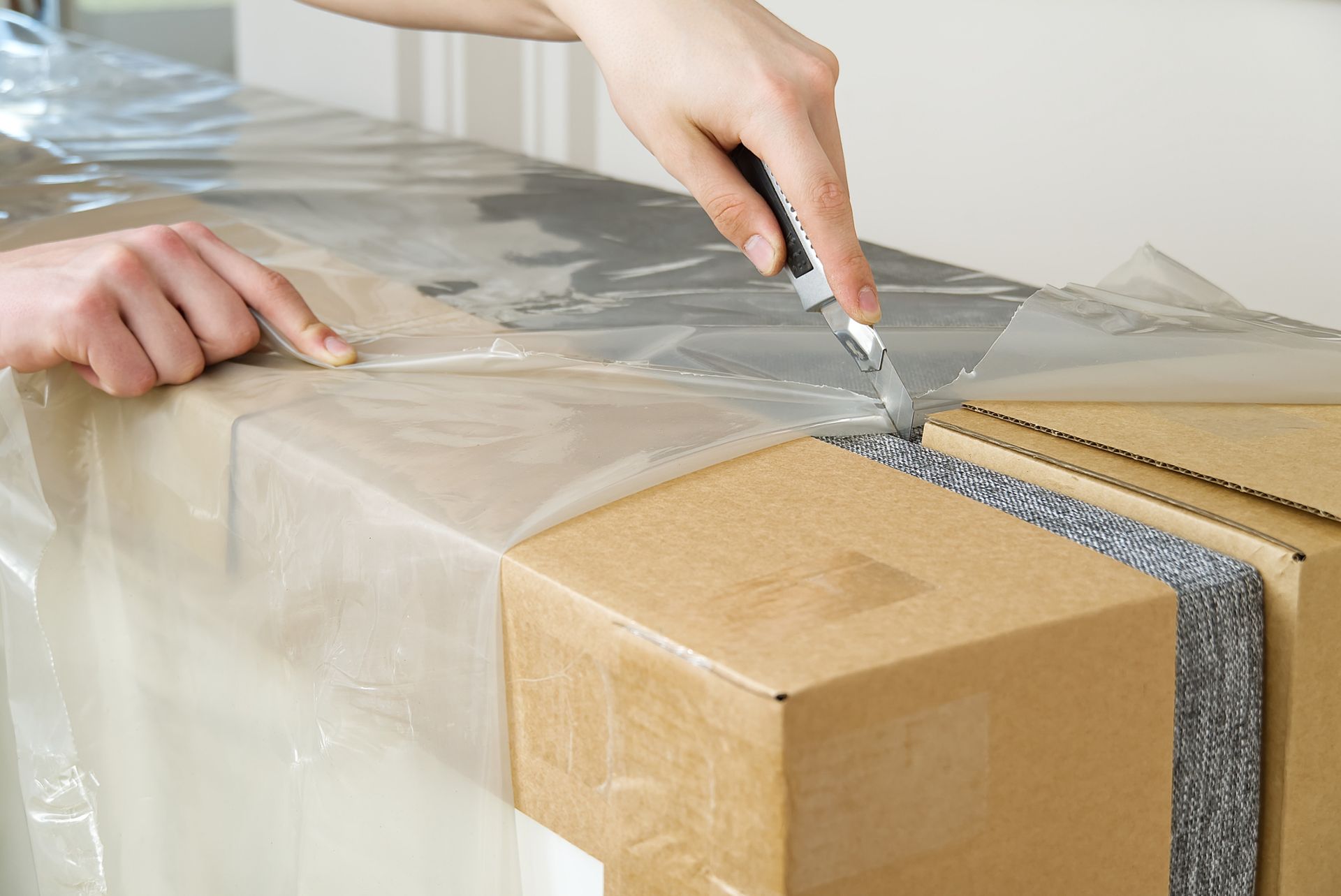 Hands wrapping a cardboard box with clear plastic and packing tape on a table