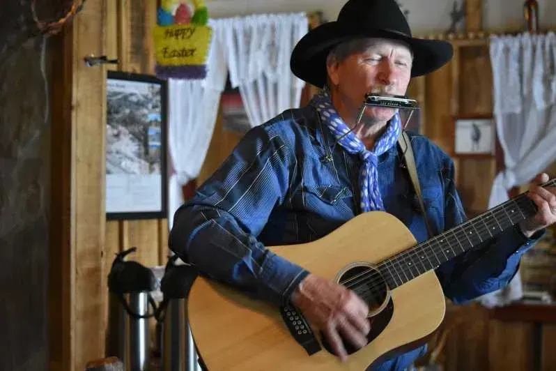 A man in a cowboy hat is playing a guitar and singing into a harmonica.