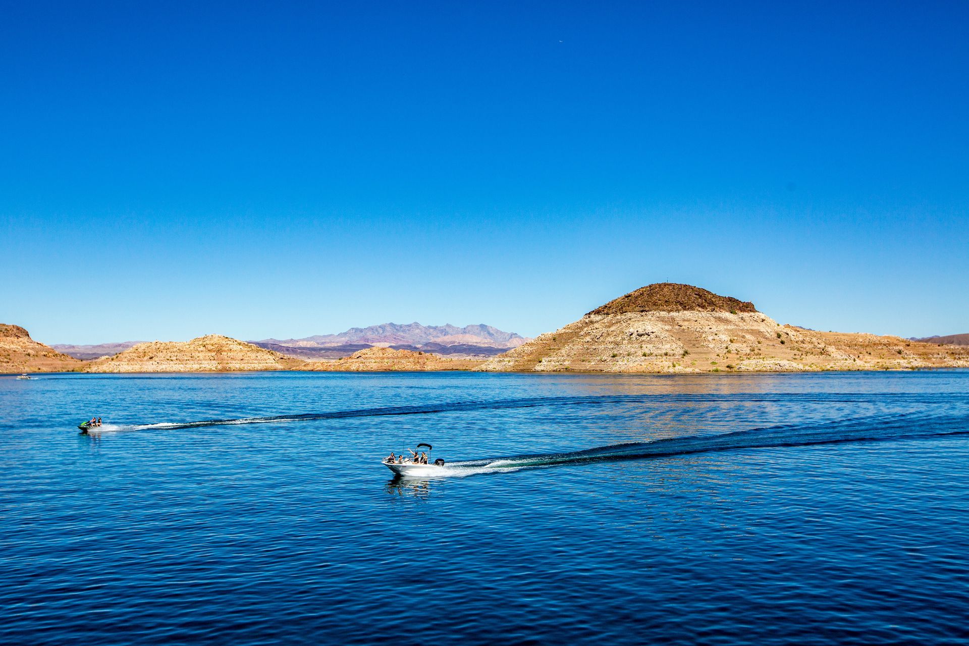 Two boats are floating on a lake with mountains in the background.
