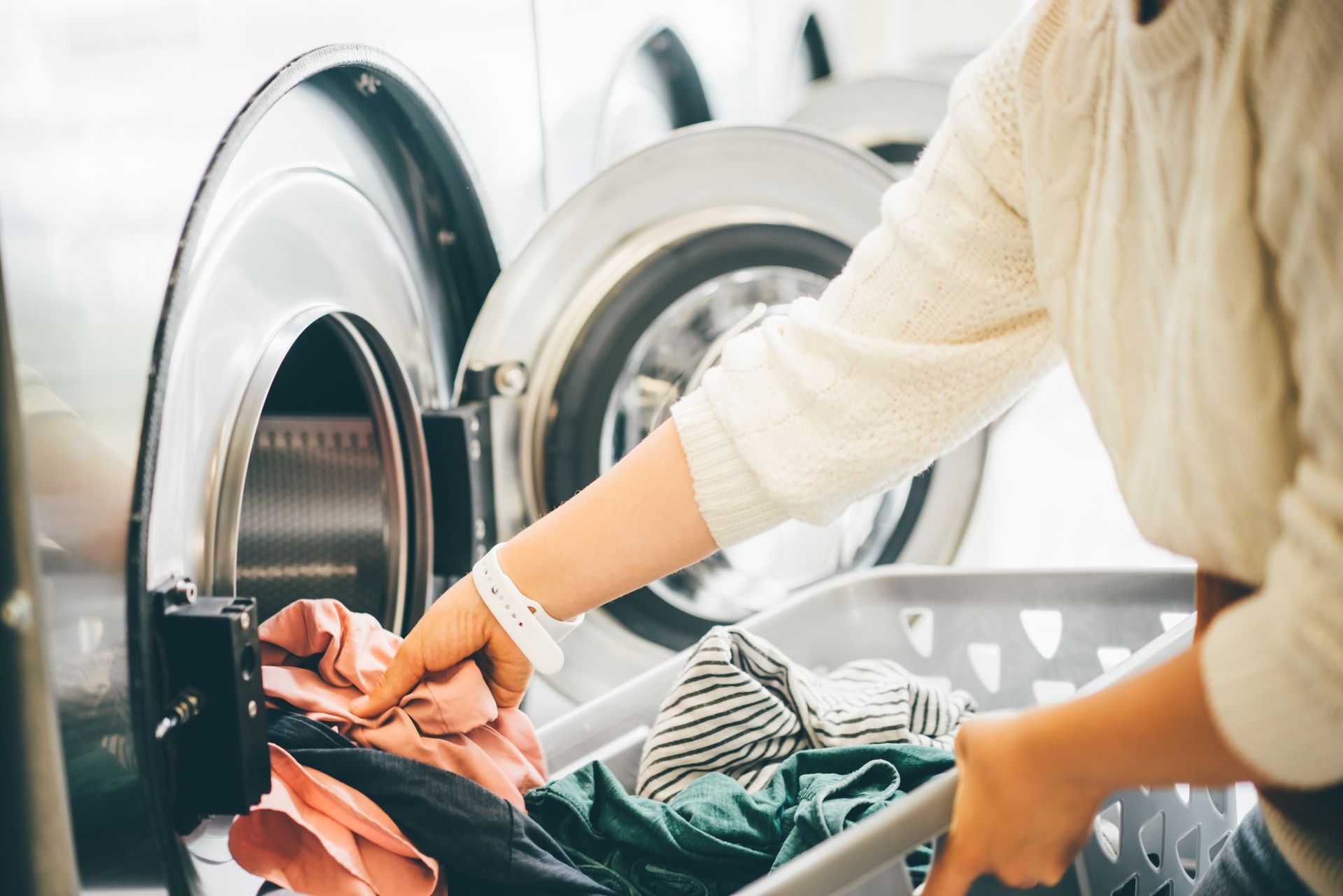 A woman is putting clothes in a washing machine.