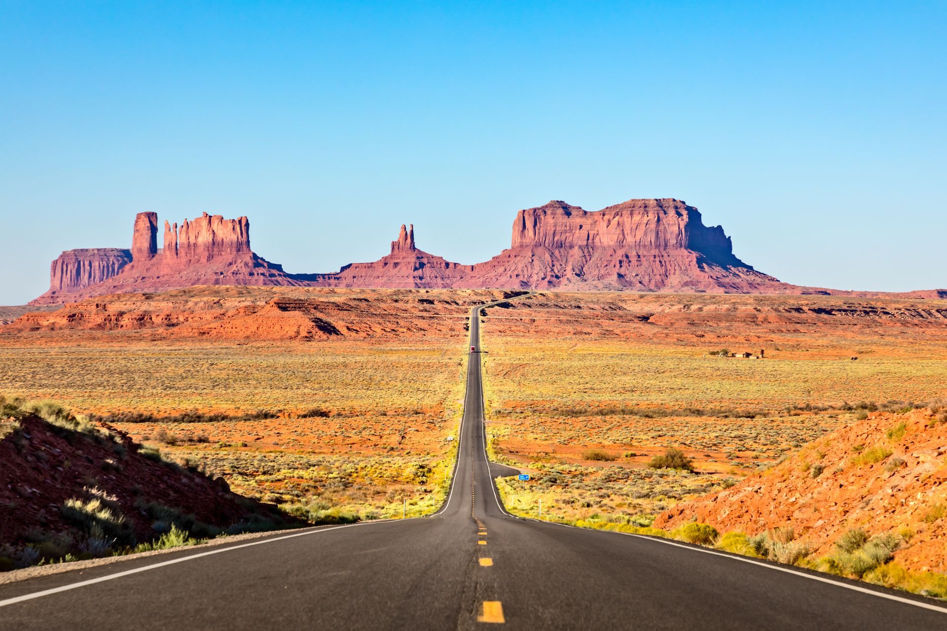 A long road in the desert with mountains in the background.