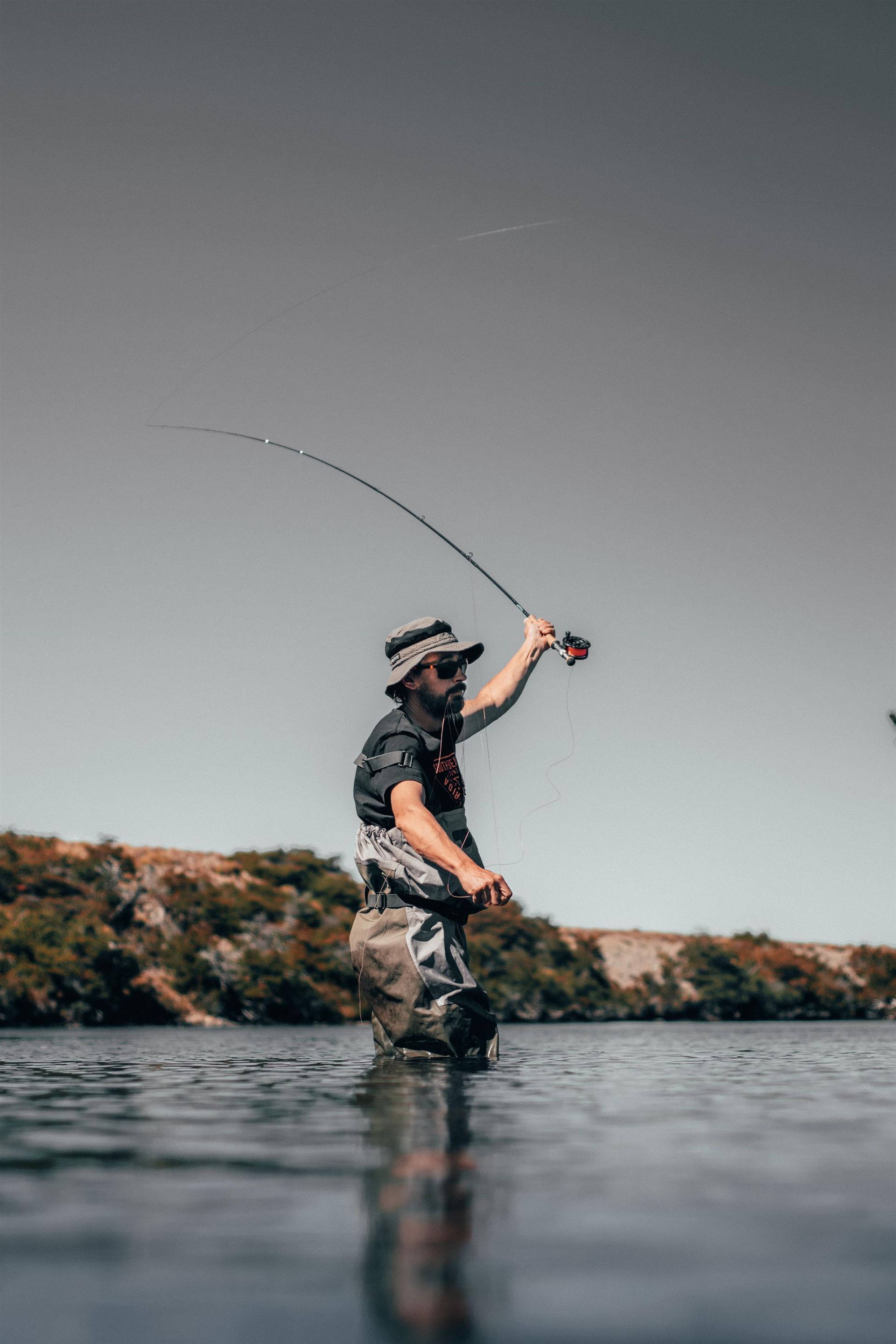 A man is kneeling in the water holding a fishing rod.