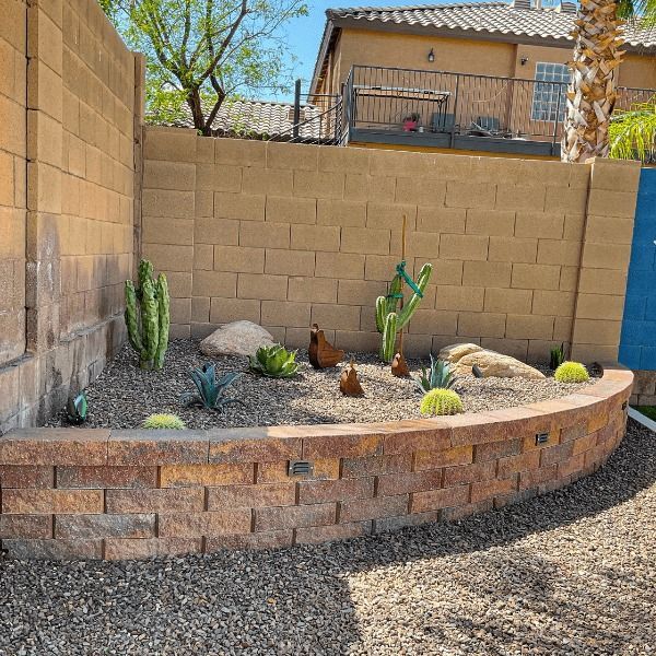 A brick wall surrounds a garden with cactus and rocks.