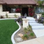 A house with a lush green lawn and a walkway leading to it.