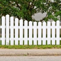 A white picket fence is sitting on the side of the road next to a tree.