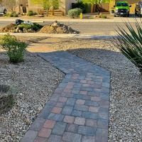 A brick walkway leading to a house with a green truck parked on the side of the road.