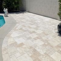 A tiled patio next to a pool with a statue in the background.
