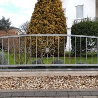 A metal fence is surrounded by trees and bushes in front of a house.