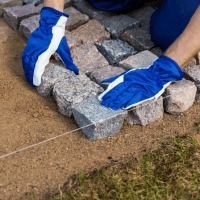 A person wearing blue gloves is laying bricks on the ground.