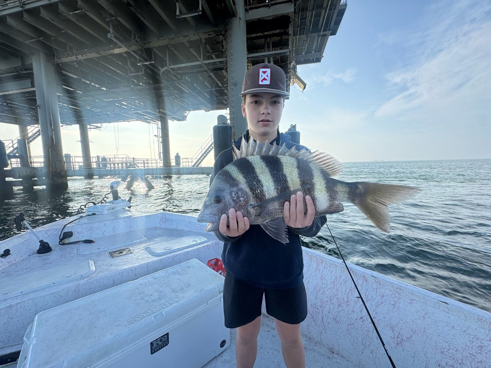 Person holding a striped fish on a boat under a bridge near the water