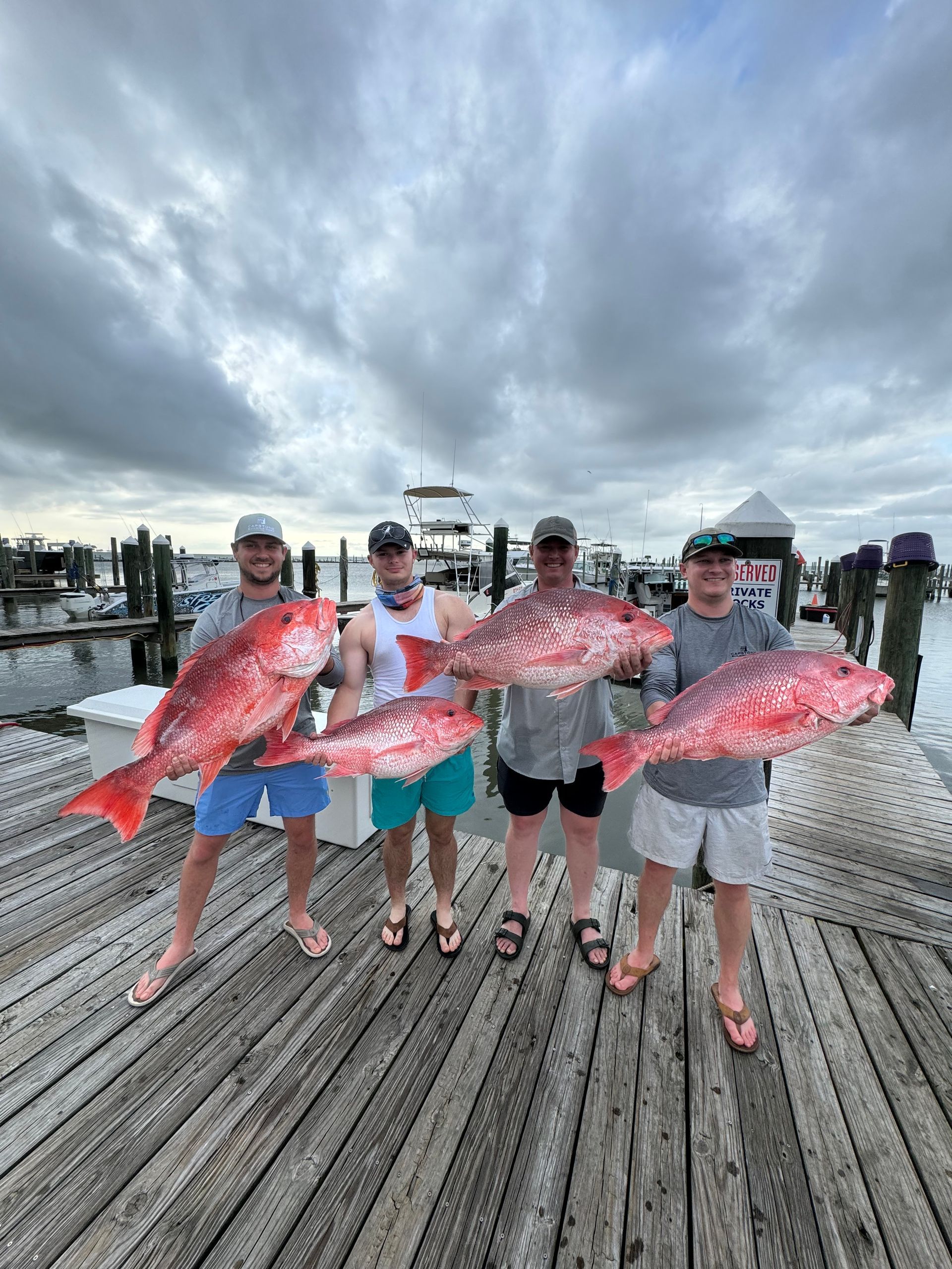Four anglers holding large pink fish on a dock under a cloudy sky