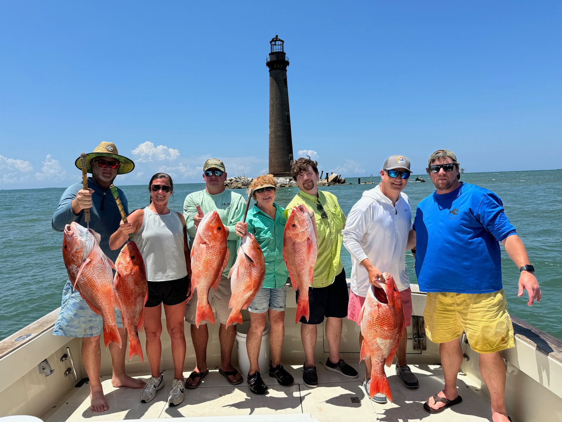 Group of anglers on a boat posing with several large fish, blue sky and sea behind them.