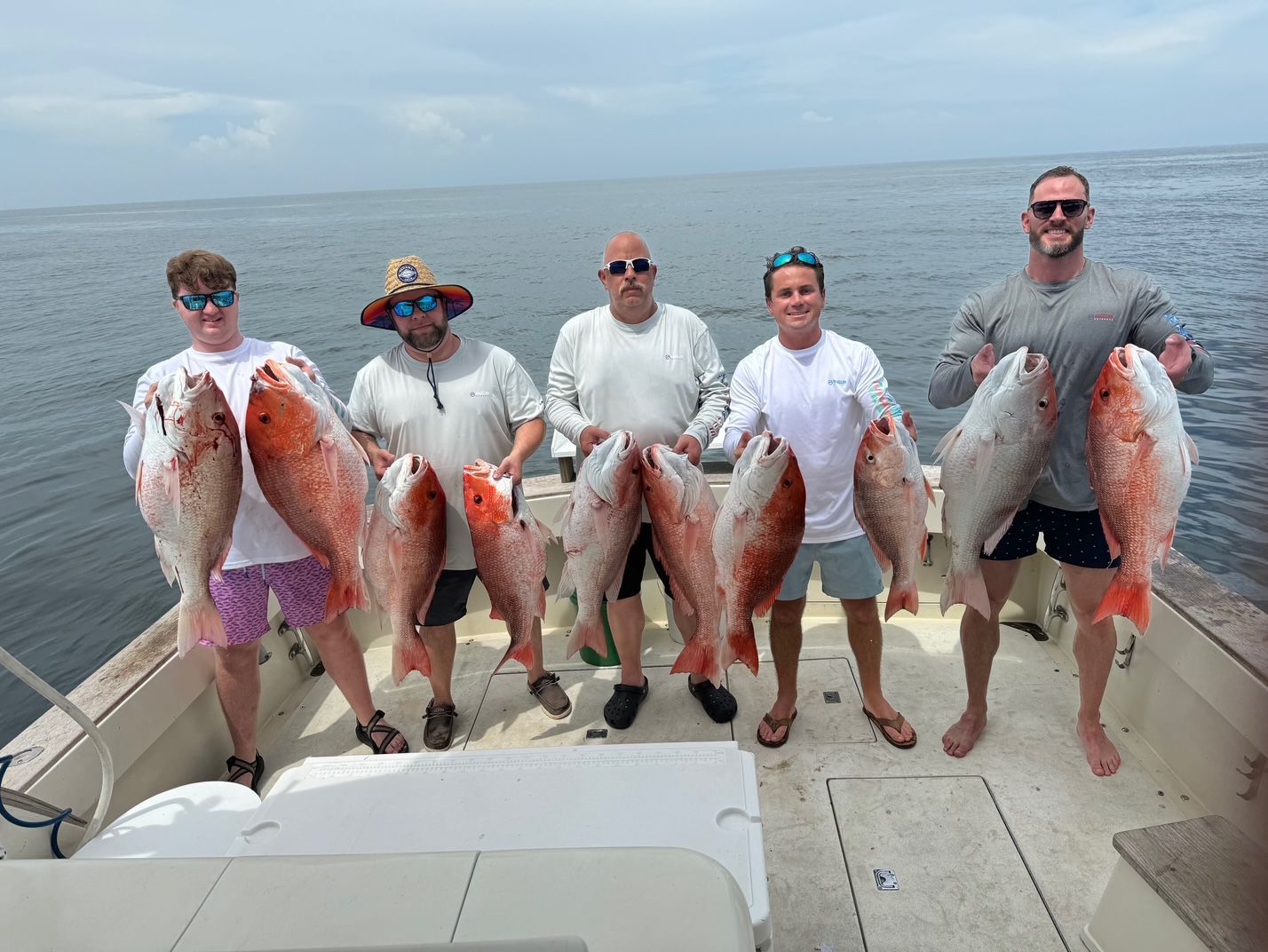 Five people holding large fish on a boat at sea under a cloudy sky