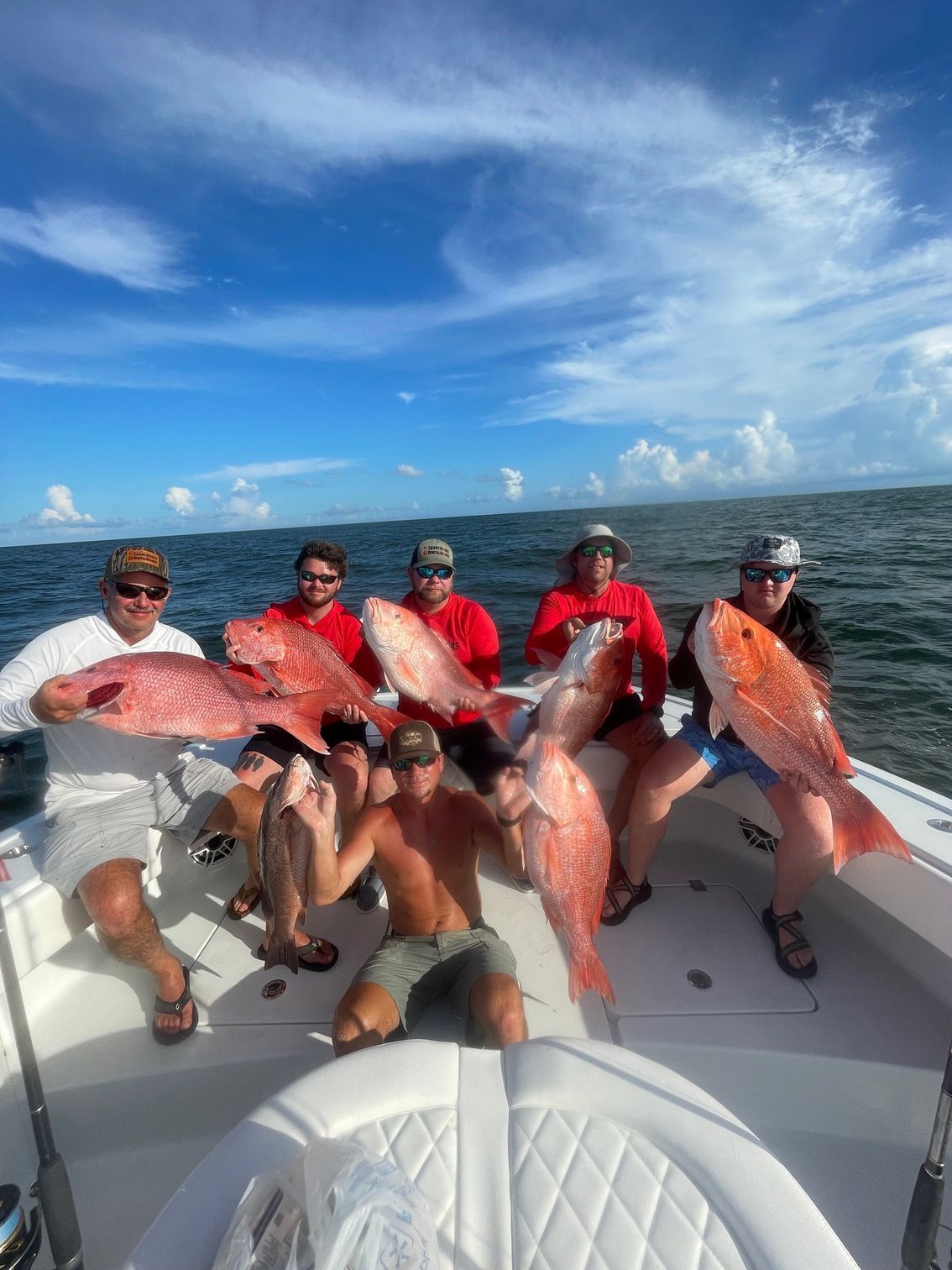 Five anglers on a boat holding large red fish on a sunny ocean trip