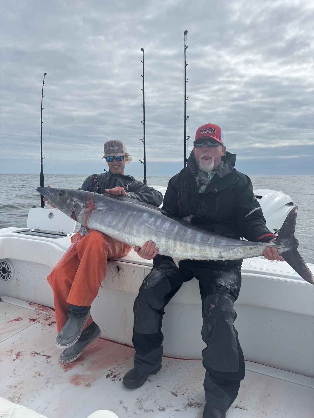 Two anglers on a boat holding a large silver fish over the ocean.