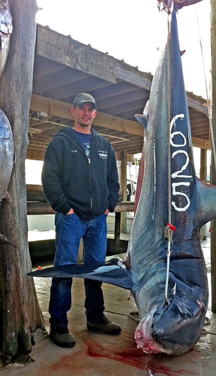 Man standing beside a hanging fish marked “625” in a fish cleaning area