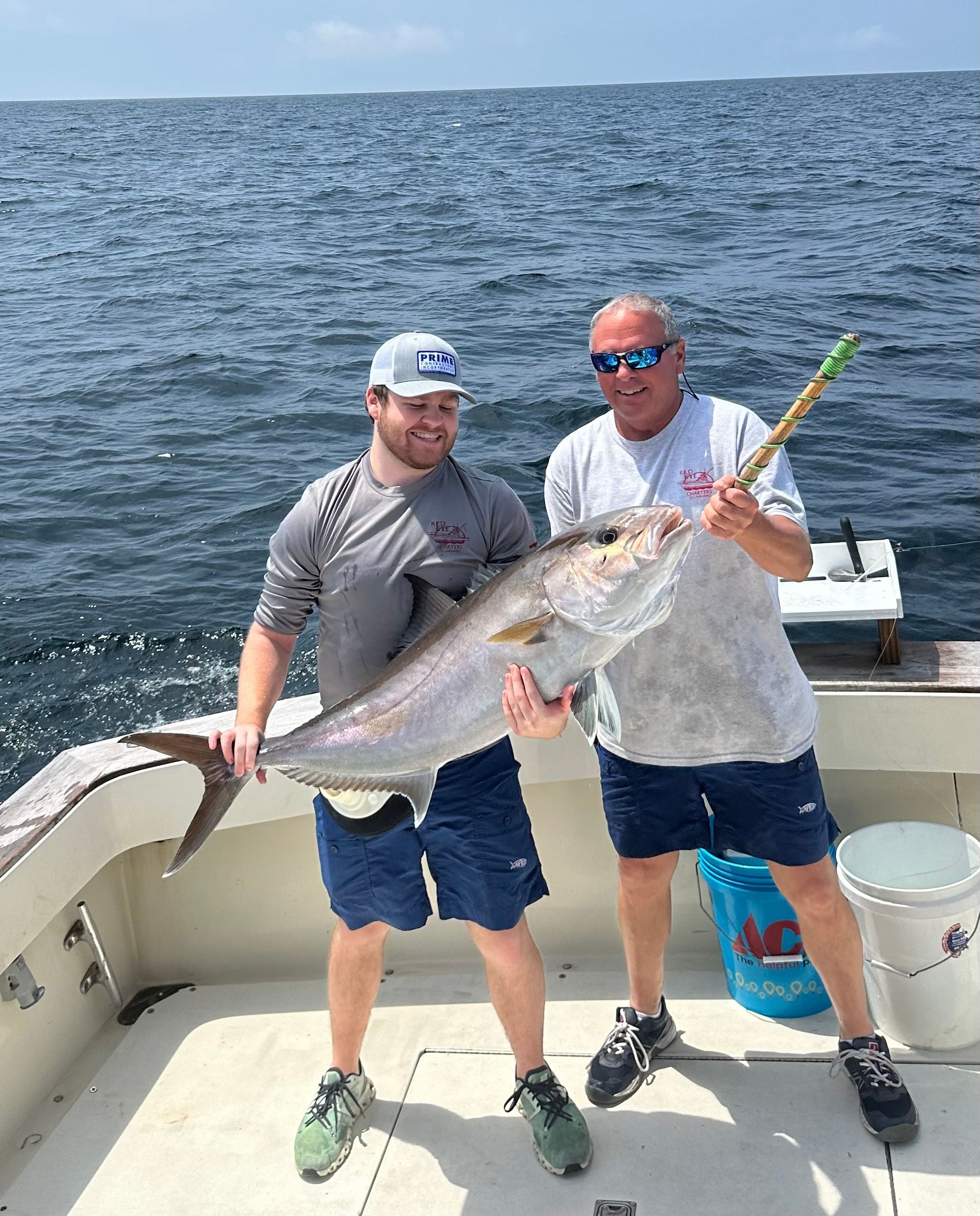 Two anglers on a boat hold up a large silver fish on a sunny day at sea.