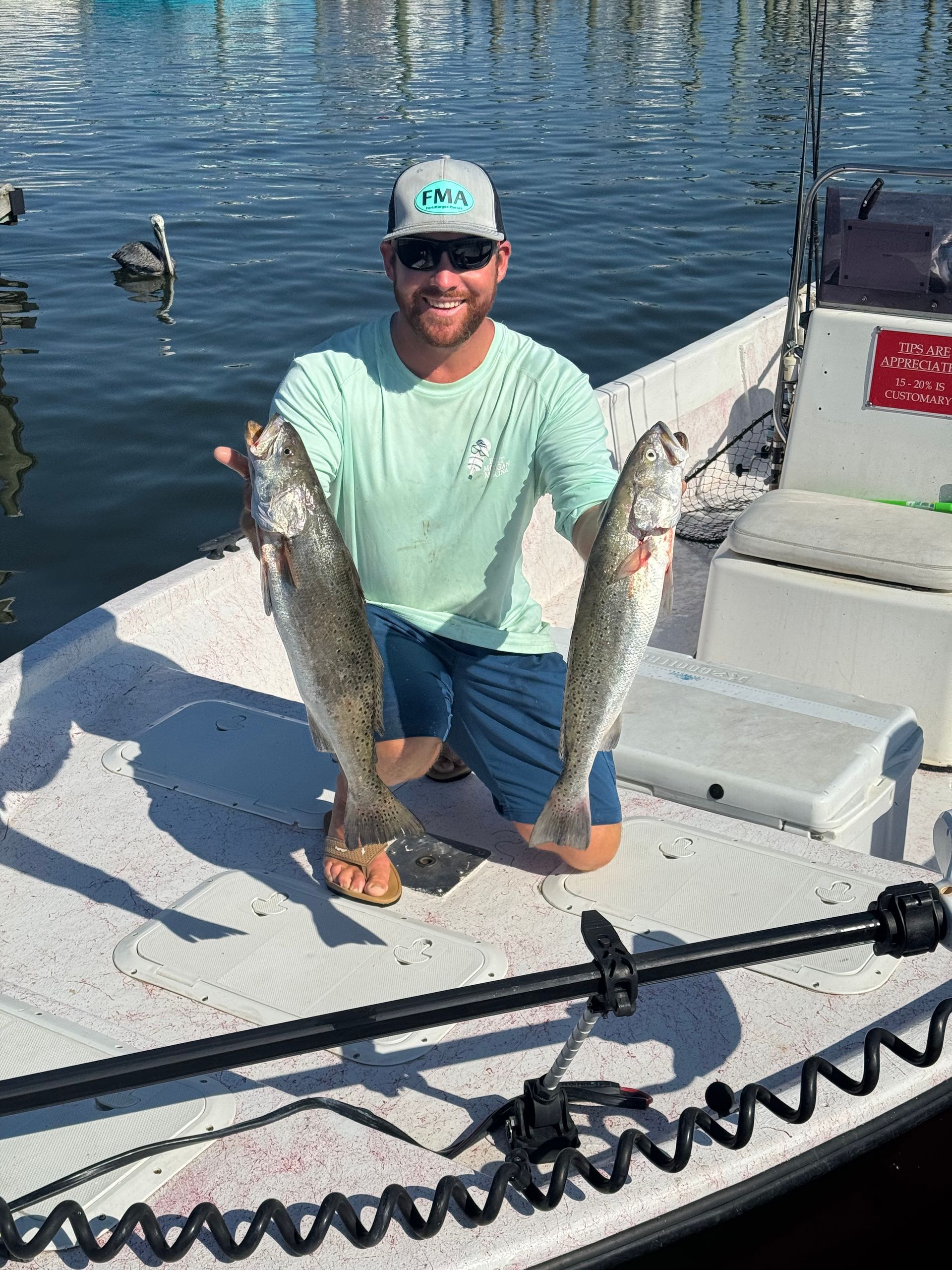 Smiling person kneeling on a boat dock, holding two large fish over the water.