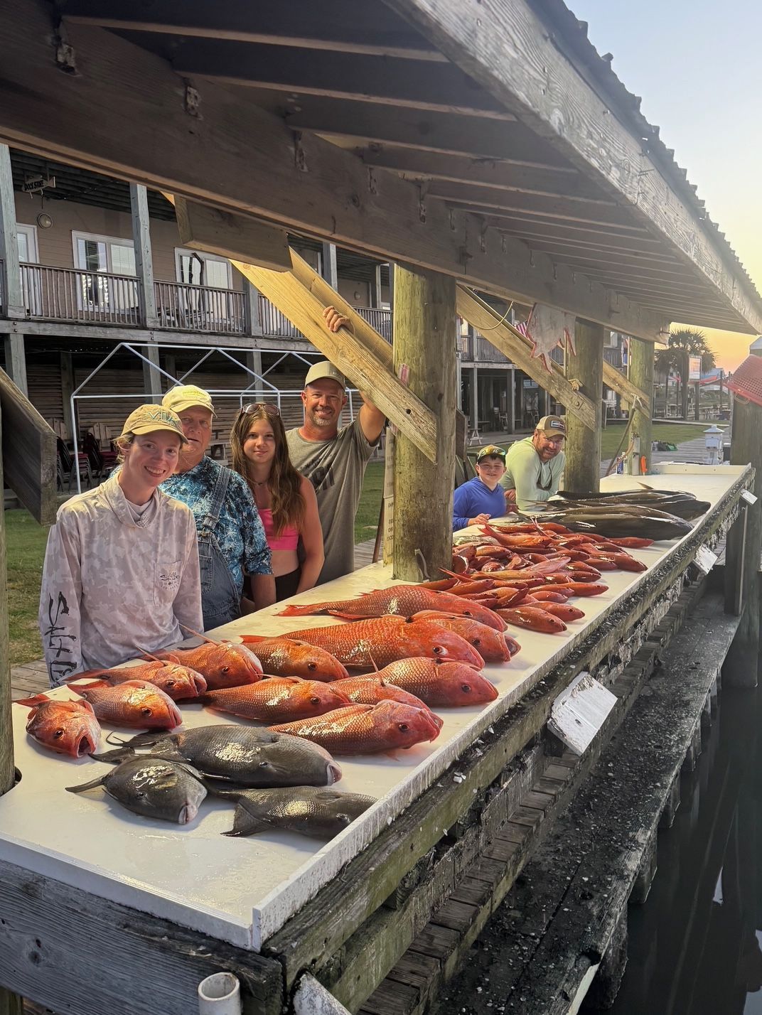 Outdoor seafood market stall with trays of shellfish and fish under a wooden roof, vendors behind the counter
