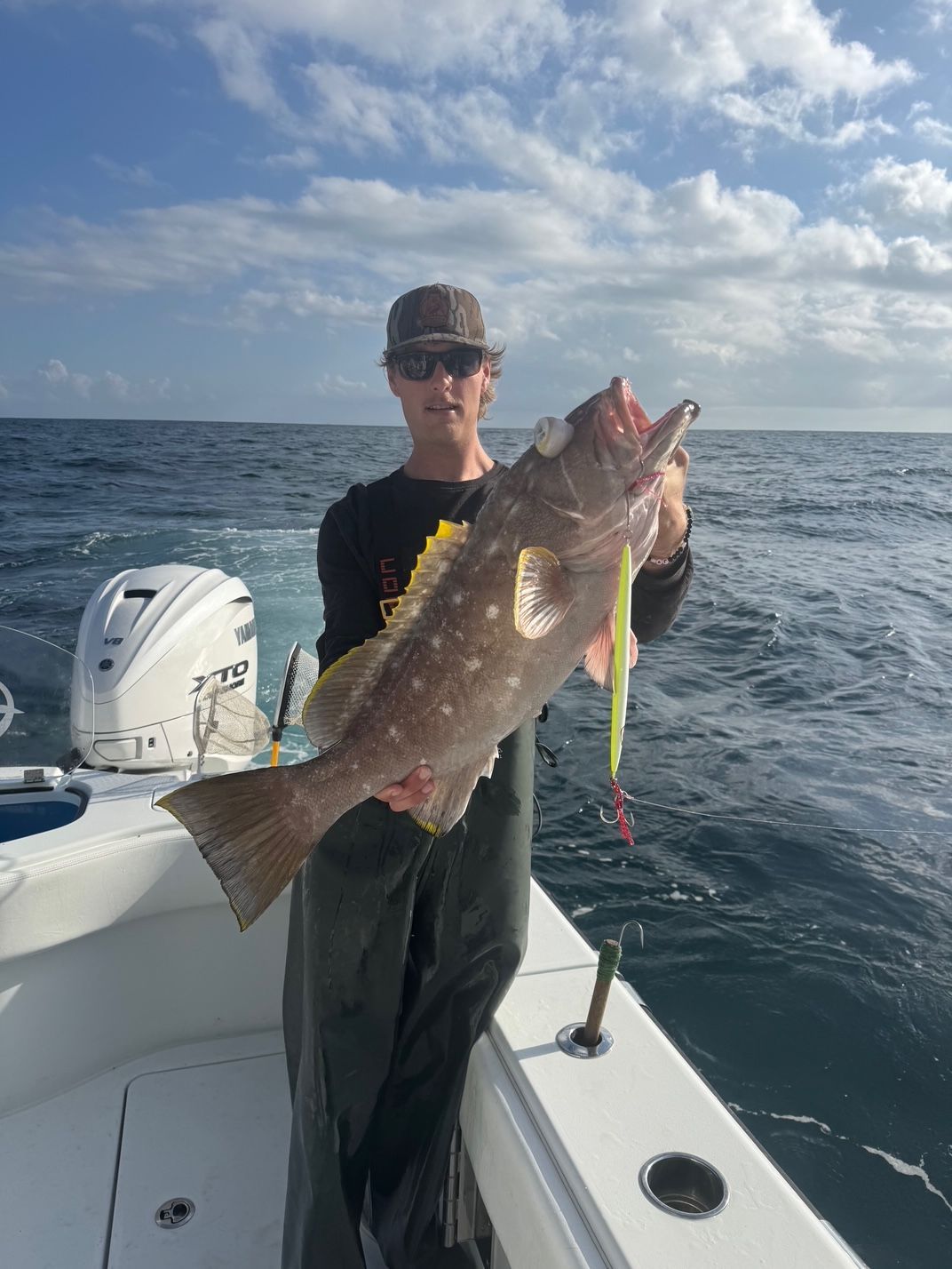 Person on a boat holding a large fish, with ocean and cloudy sky in the background.