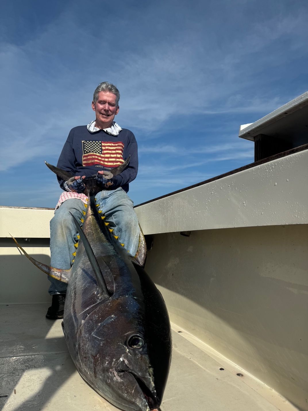 Man sitting on a boat holding a large fish under a blue sky.