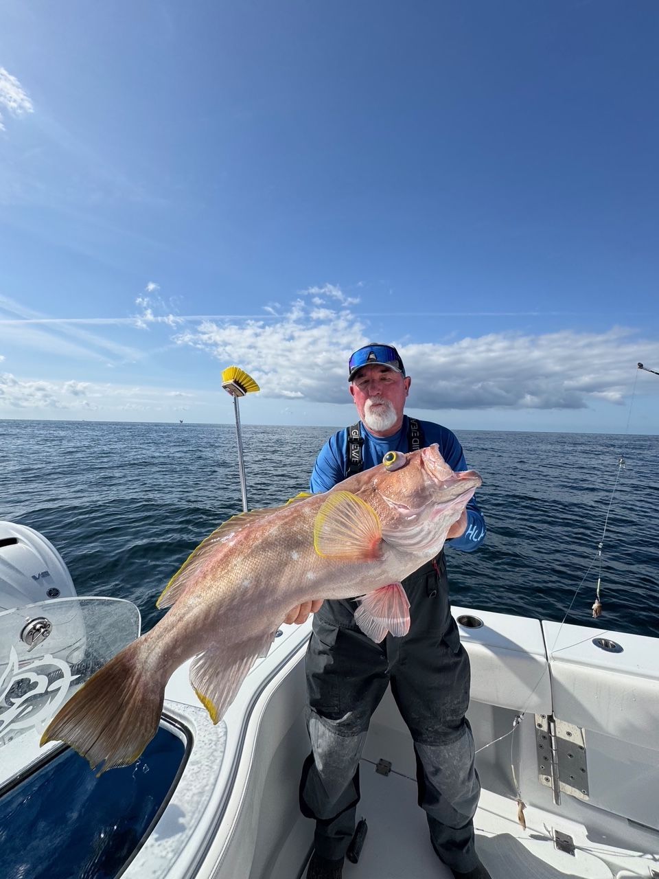 Man on a boat holding a large fish on a sunny open sea.