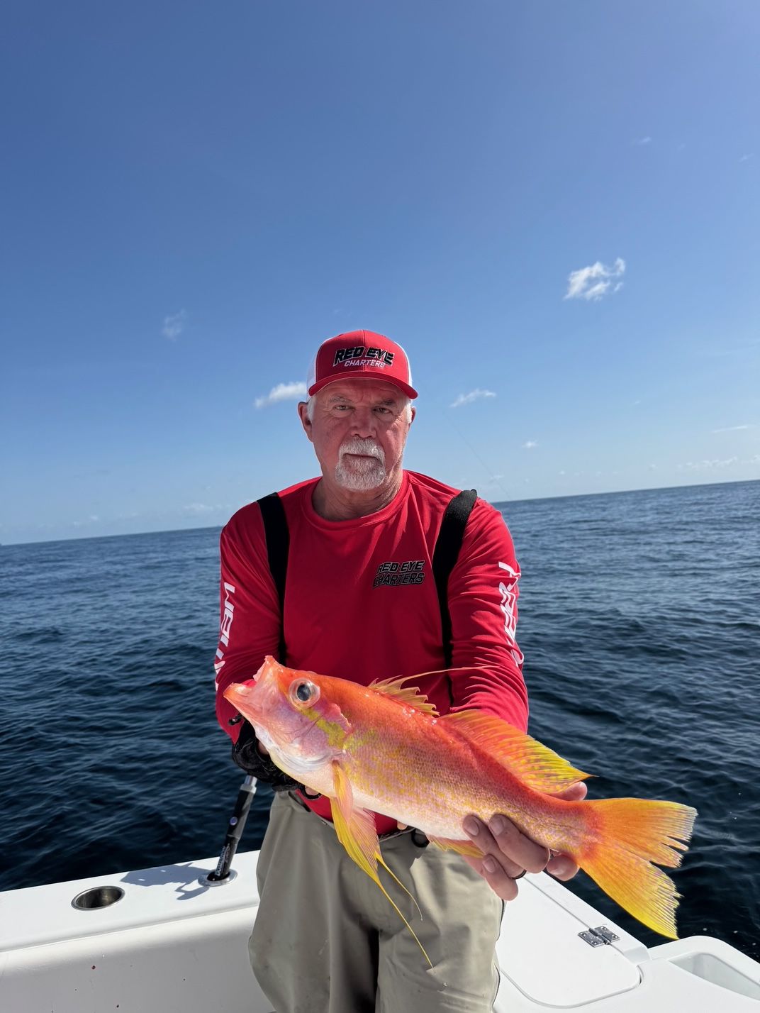 Man holding a bright orange fish on a boat at sea under a clear blue sky