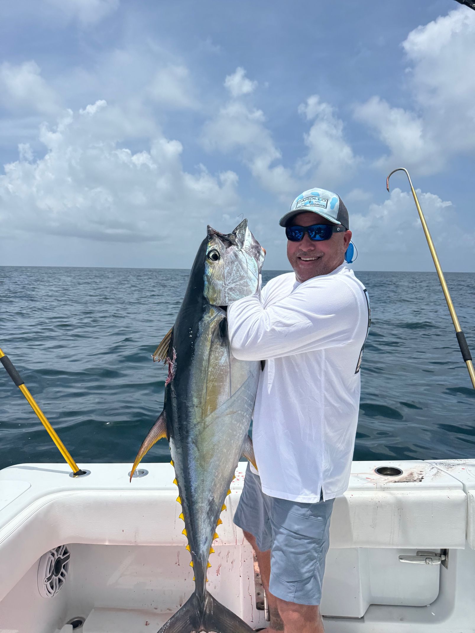 Angler on a boat holds a large yellowfin tuna at sea under a cloudy sky.