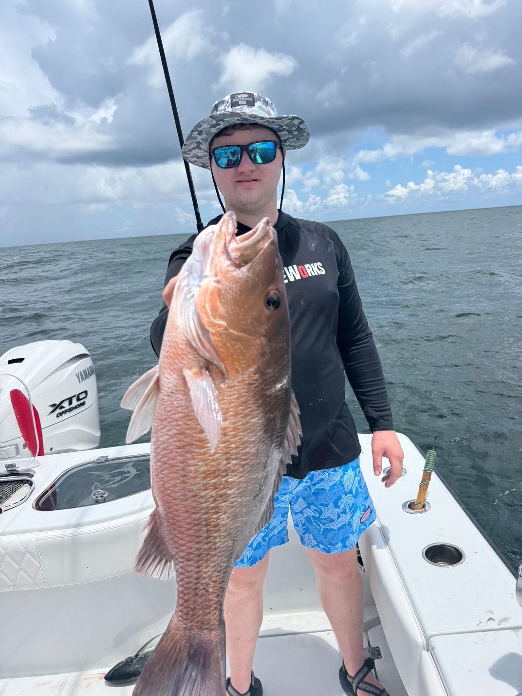 Angler on a boat holding a large red fish on the open water.
