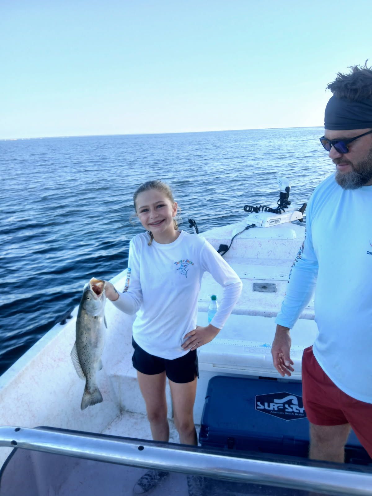 Two people on a boat, one holding a large fish with ocean water in the background.
