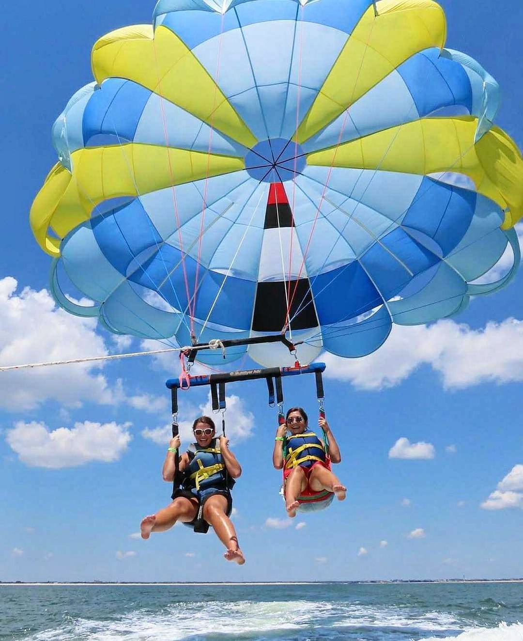 Two people parasailing over ocean, blue sky, yellow and blue parachute.