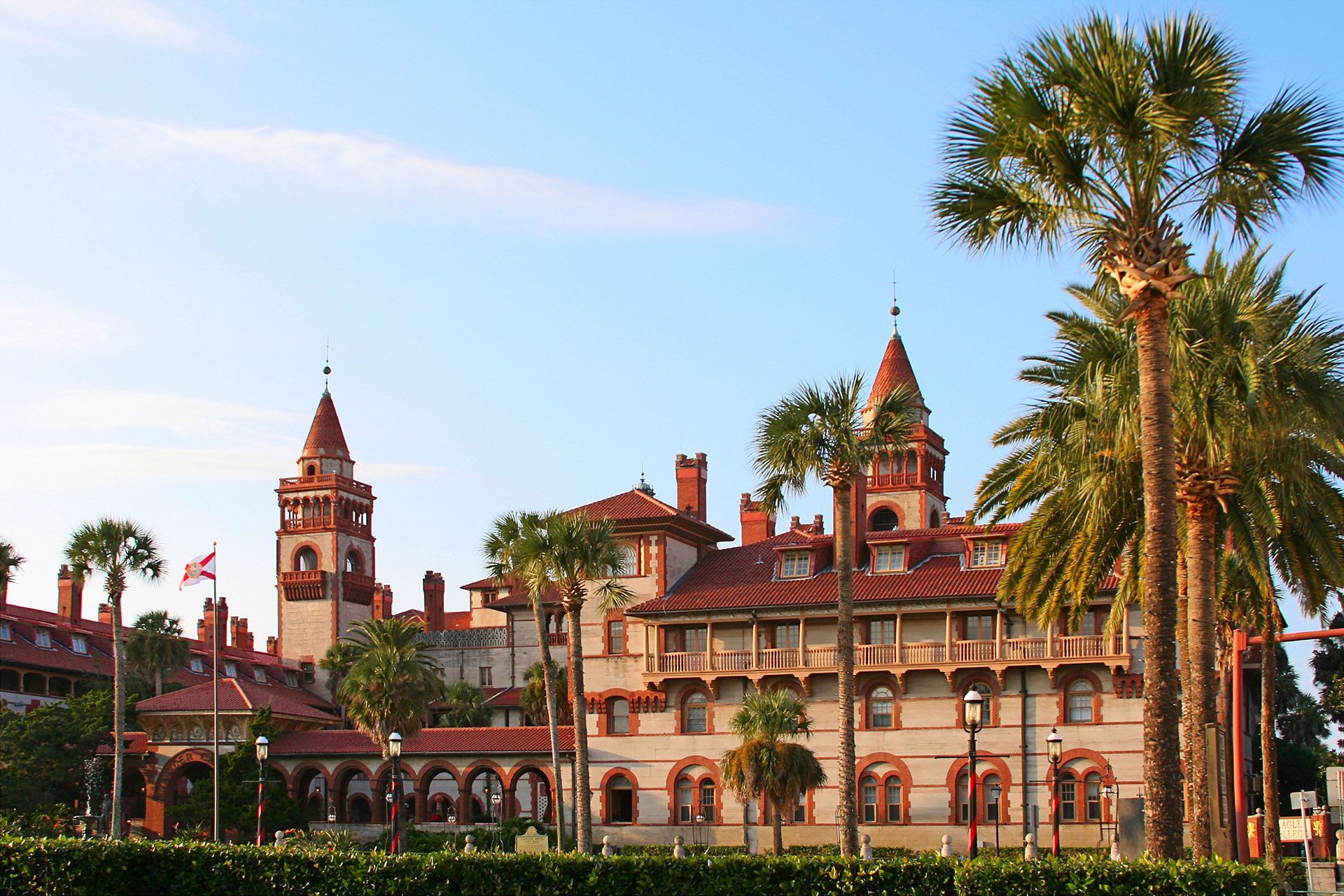 Historic building with red roofs, towers, and palm trees in St. Augustine, Florida, against a blue sky.