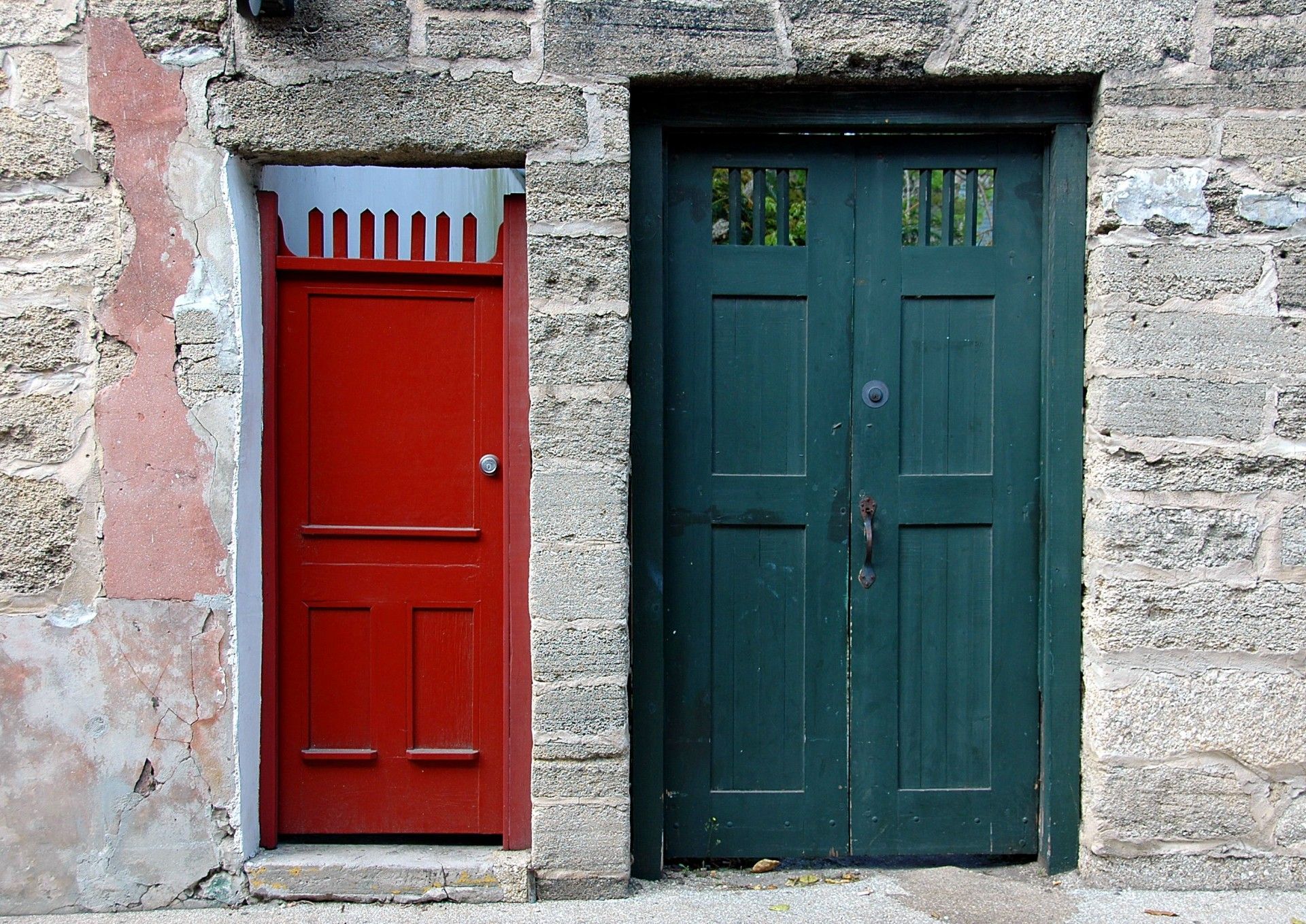 Red door next to green door in stone wall.