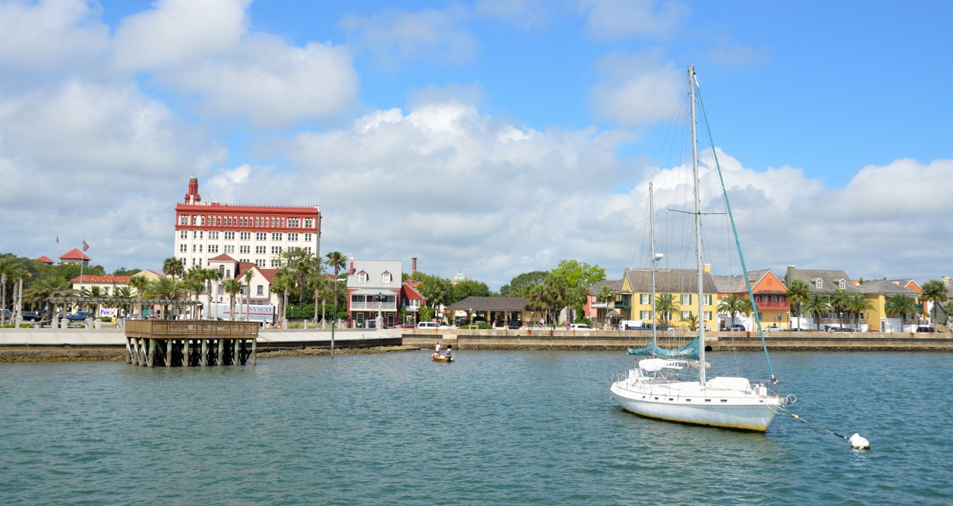 View of St. Augustine, Florida, waterfront with a white sailboat on the water and buildings with red roofs.